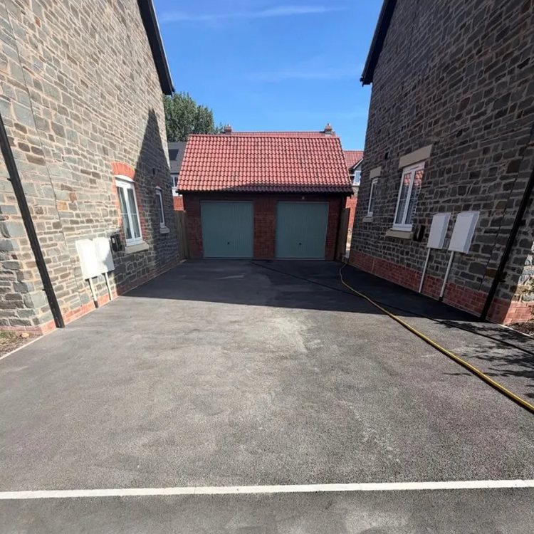 Tarmac driveway between two stone houses before restoration, faded and grey